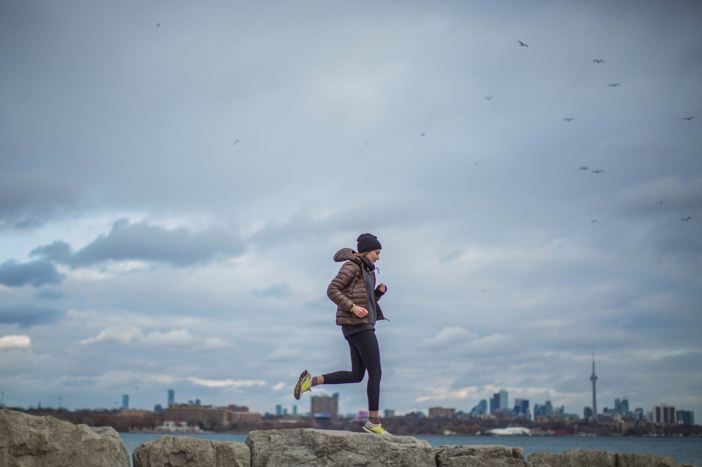 A runner jogging along a city waterfront under a cloudy sky.